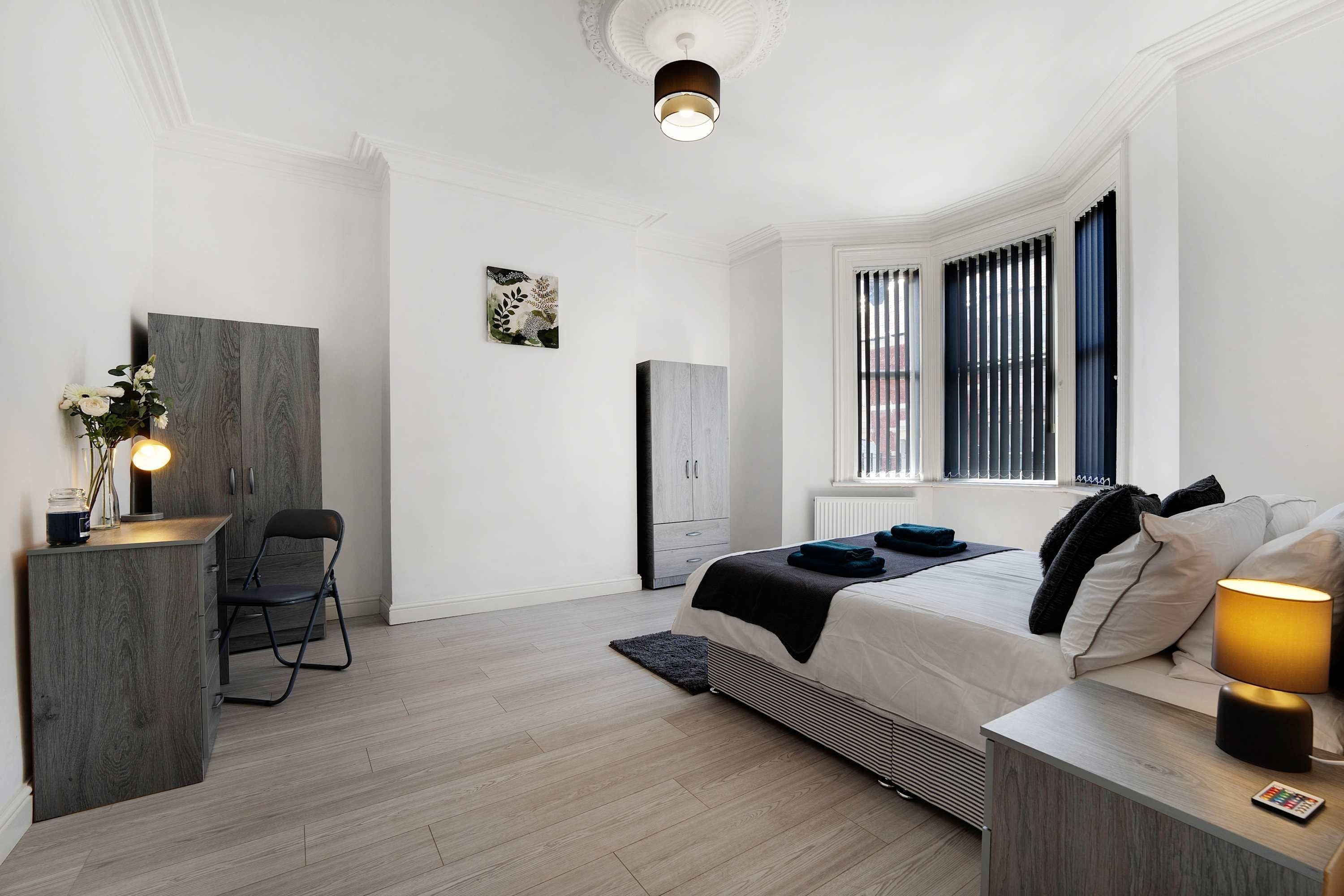 Un dormitorio moderno con cama, mesita de noche, lámpara y escritorio con silla.
