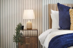 A neatly made bed with a headboard, a bedside lamp, a small wooden nightstand with drawers, and a potted plant. - Spacious Two-storey 4BR Eston Home Sleeps 8 (Middlesbrough)