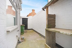 A narrow alleyway with white brick walls, a green trash bin, and a black door. - Spacious Two-storey 4BR Eston Home Sleeps 8 (Middlesbrough)