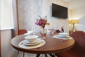 A dining table set for four with a vase of flowers, a flat-screen TV mounted on the wall, and a lamp on the side. - Spacious Two-storey 4BR Eston Home Sleeps 8 (Middlesbrough)