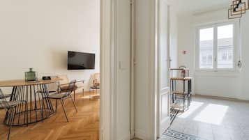 Een kamer met een houten visgraatvloer, een eettafel met stoelen, een flatscreen televisie aan de muur en een raam met uitzicht op gebouwen.