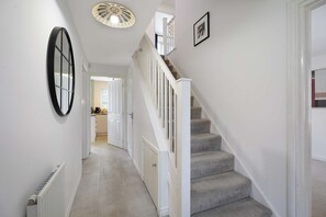 A hallway with a staircase, white walls, a radiator, and a door leading to another room. - Modern 4BR Stay Driveway Parking By Stay With Us (Middlesbrough)