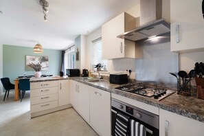 A modern kitchen with a gas stove, a dishwasher, and a dining area with a table and chairs. - Modern 4BR Stay Driveway Parking By Stay With Us (Middlesbrough)