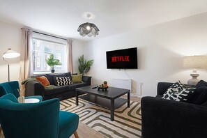 Un salon moderne comprenant un canapé, des fauteuils, une table basse et un téléviseur à écran plat fixé au mur.