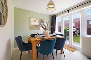 Un coin repas avec une table dressée pour quatre personnes, des chaises, un vase contenant des plantes séchées et un tableau accroché au mur.