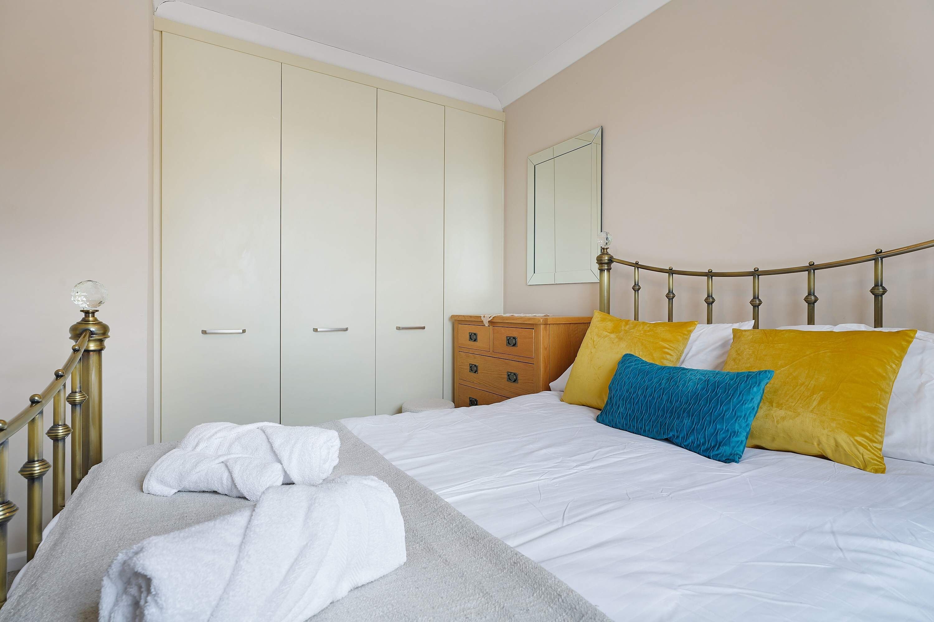 A bedroom with a bed, a wooden dresser, a wardrobe, and a mirror on the wall.