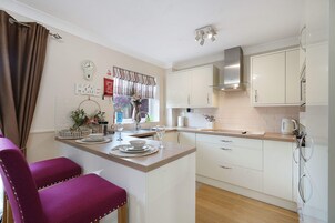 A modern kitchen with white cabinets, a wooden countertop, and a dining area with a purple chair.