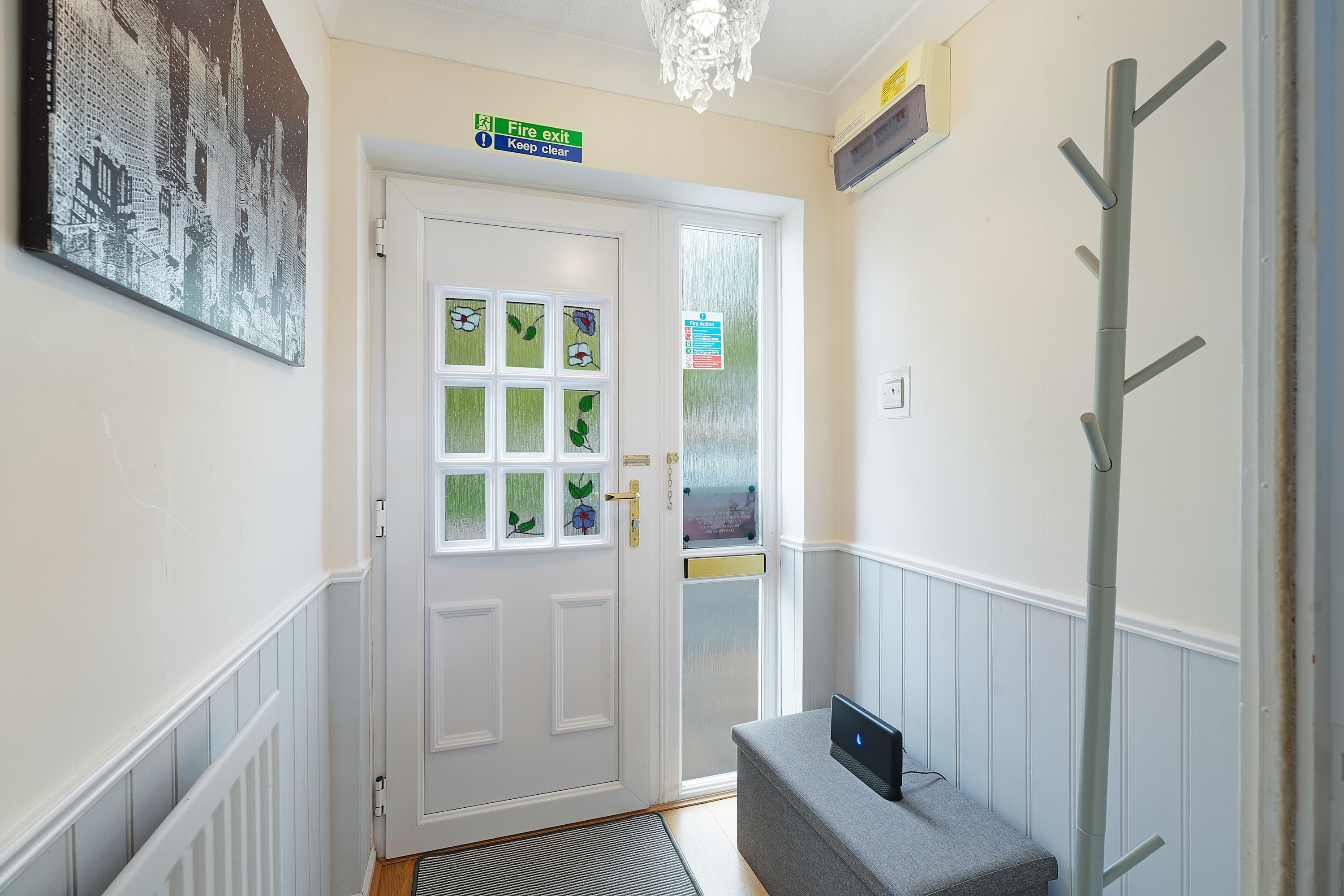 A hallway with a white door, a fire exit sign, a fire action sign, and a coat rack.