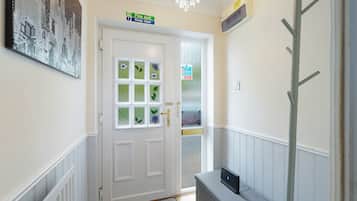 A hallway with a white door, a fire exit sign, a fire action sign, and a coat rack.