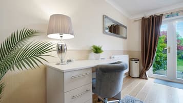 Ein modernes Zimmer mit Schreibtisch, Stuhl, Lampe, Spiegel, Topfpflanze und Blick ins Freie.