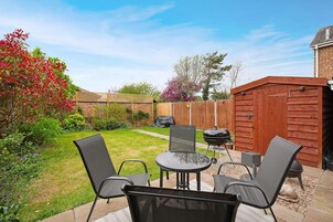 Un patio trasero con zona de terraza, una parrilla y un cobertizo de madera.
