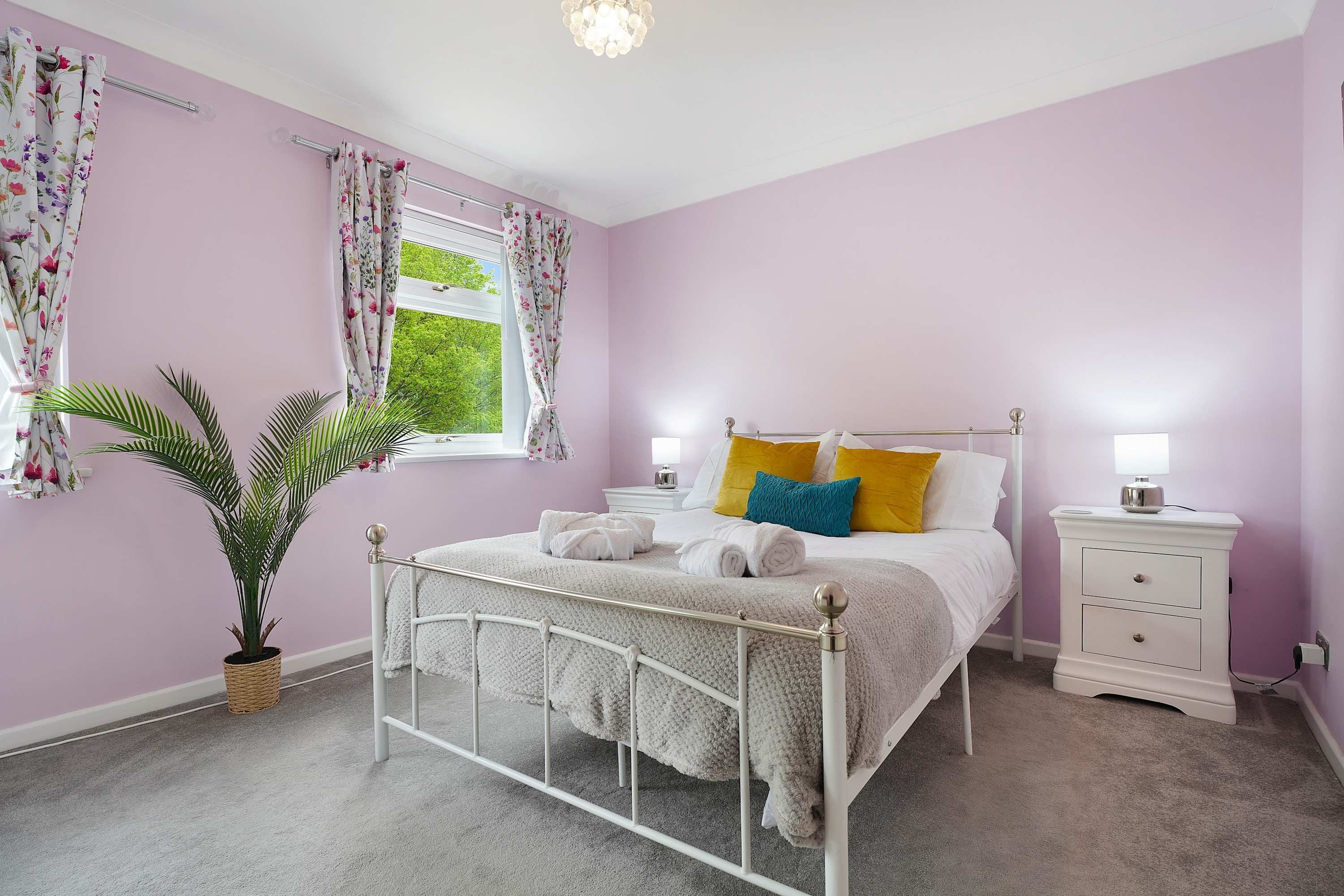 A bedroom with a bed, bedside tables, a potted plant, and a window with curtains.