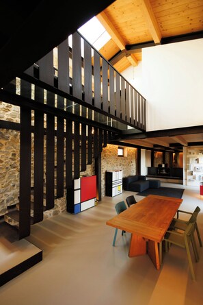 A spacious interior with a high ceiling, a wooden dining table, and a stone wall. - Historic Tuscan farmhouse with double-height hall (Montemurlo)