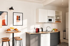 Eine moderne Küche mit integriertem Mikrowellenherd, Spüle und kleinem Kühlschrank. Ein Frühstücksbuffet mit Croissants und Orangensaft steht auf einem Holztisch bereit.