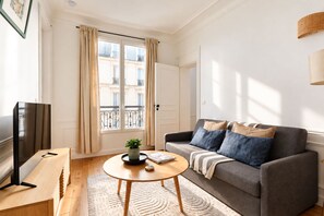 Ein Wohnzimmer mit einer Couch, einem Couchtisch, einem Fernseher und einem Fenster mit Vorhängen.