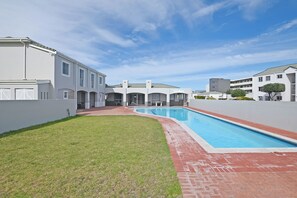 Um edifício residencial com piscina, gramado e caminho de tijolos.