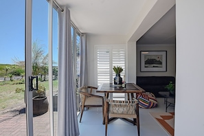 A dining area with a table and chairs, a vase with flowers, and a painting on the wall. - Stylish 2-bedroom apartment in enchanting Big Bay neighborhood (Cape Town)
