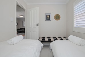 A room with two beds, a bench, a door, and a window with blinds. - Stylish 2-bedroom apartment in enchanting Big Bay neighborhood (Cape Town)