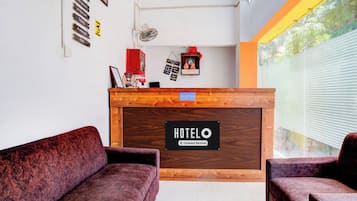 A reception desk with a sign reading 'HOTELO Company-Serviced' and a 'RECEPTION' sign above it. There are two plush armchairs in front of the desk.