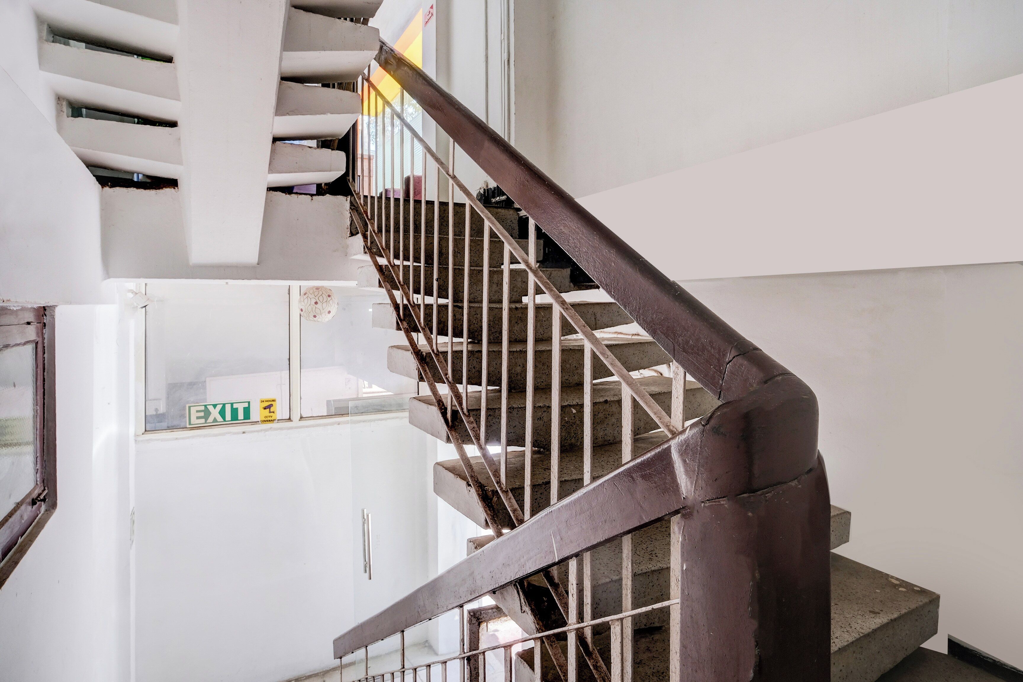 A staircase with a metal handrail and a white wall with an exit sign.