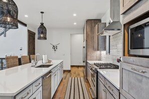 Une cuisine moderne avec des meubles blancs, une cuisinière en acier inoxydable et un luminaire suspendu.