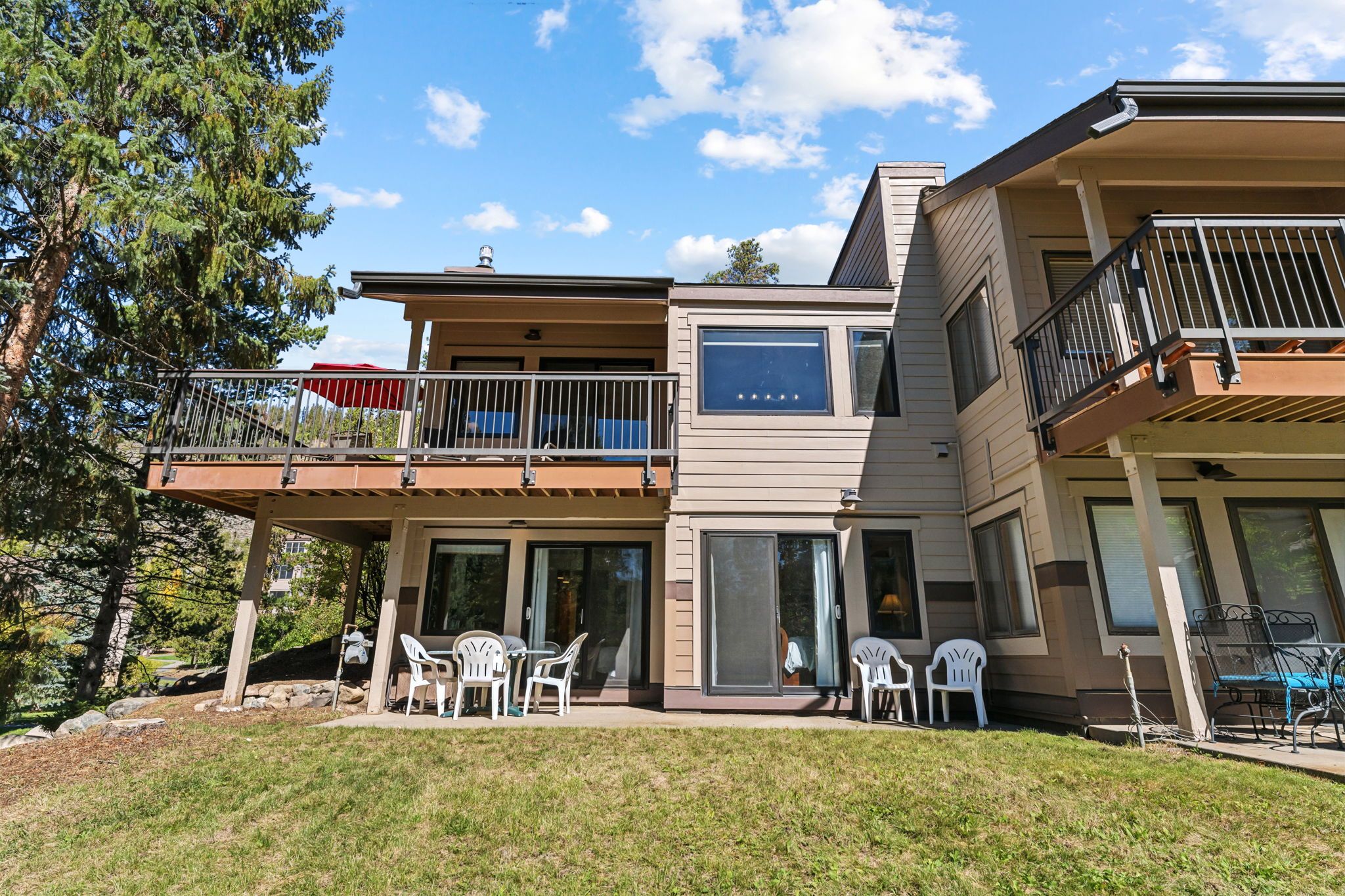 A modern two-story house with a balcony, outdoor seating, and a large sliding glass door.