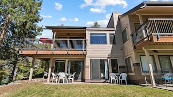 A modern two-story house with a balcony, outdoor seating, and a large sliding glass door.