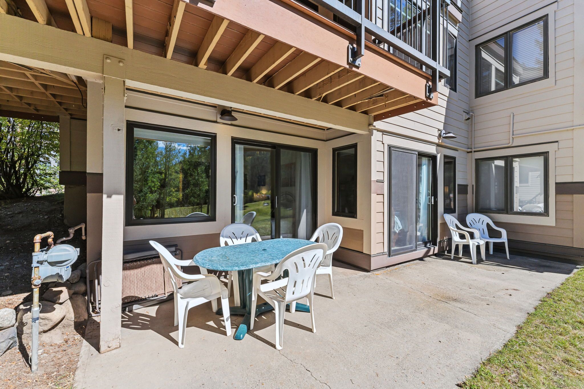 Une terrasse couverte avec une table et des chaises, de grandes fenêtres et un bâtiment doté d’un balcon.