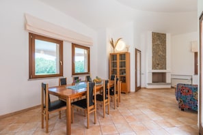 A dining area with a wooden table and chairs, a cabinet with glass doors, and a fireplace. - Villa With Private Pool Costa Rei (Muravera)