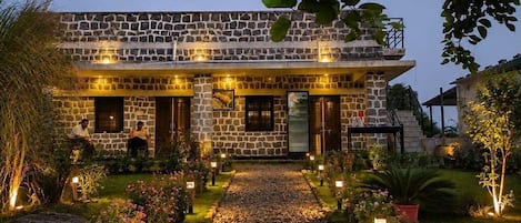 Un edificio de piedra con un sendero empedrado que lleva a la entrada, rodeado de vegetación e iluminación exterior.