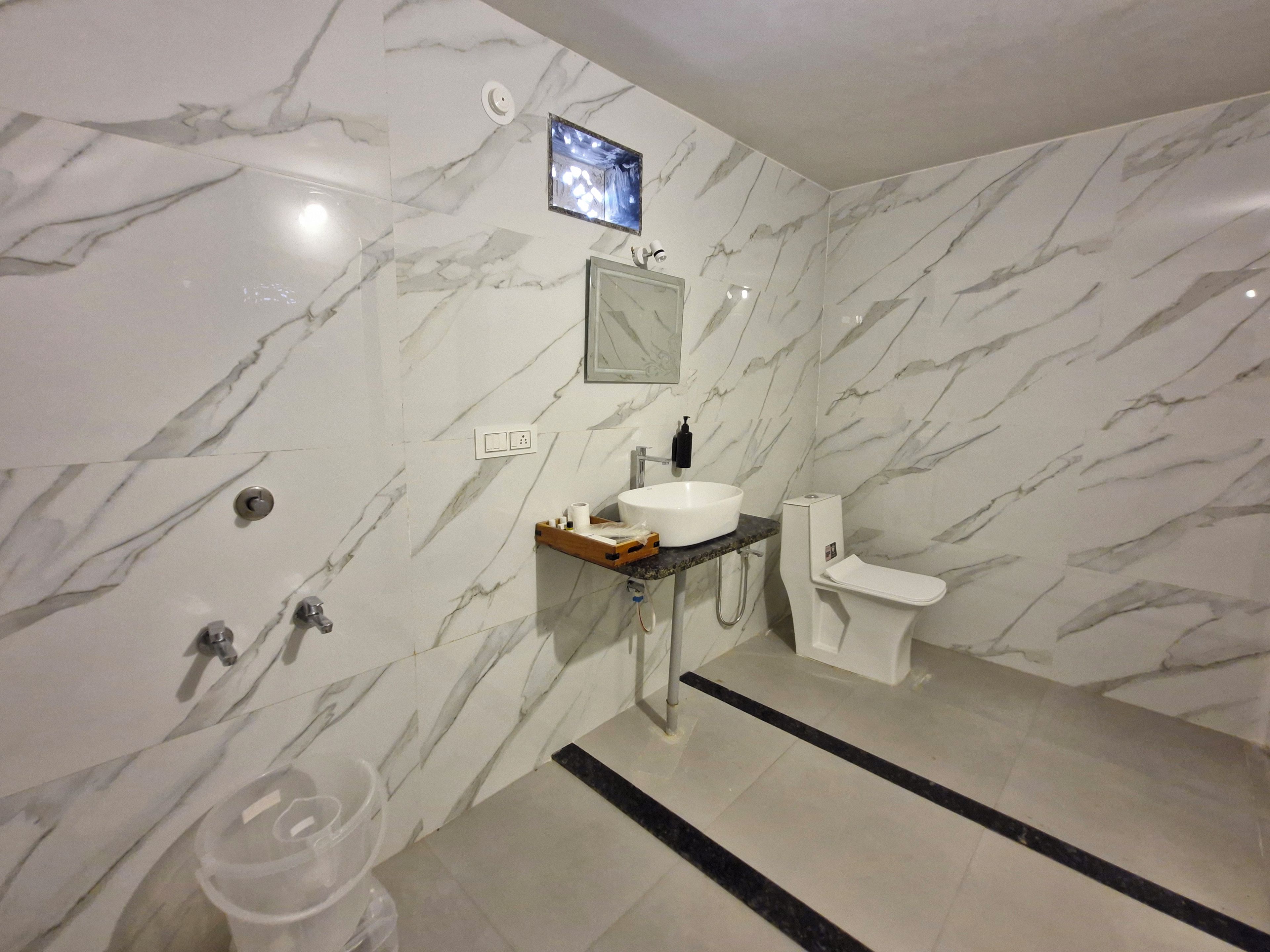 A bathroom with a marble wall, a white sink, a toilet, and a shower.
