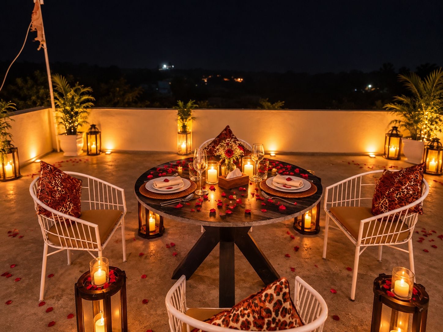 A round table set for two with candles, a vase with flowers, and a view of the night sky.