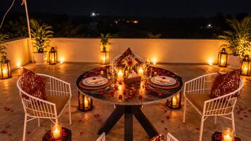 A round table set for two with candles, a vase with flowers, and a view of the night sky.