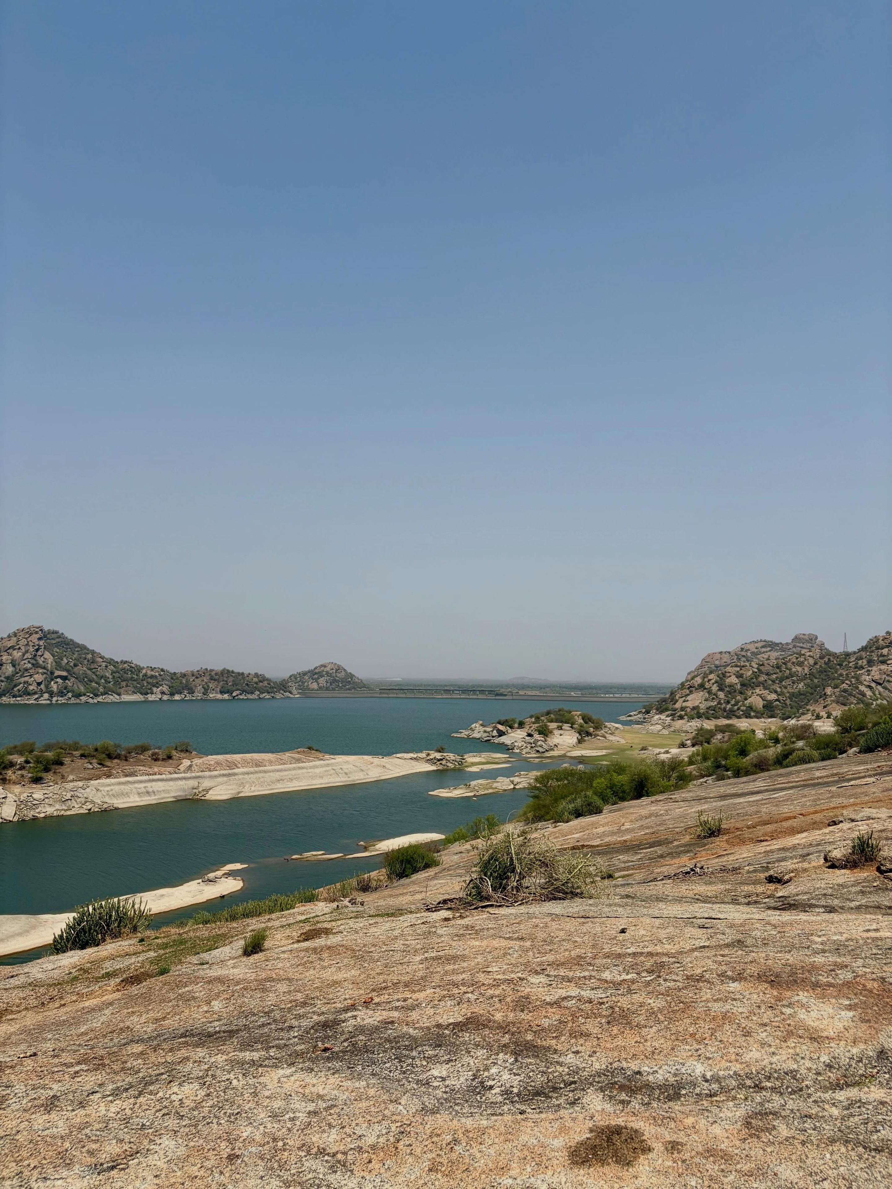 A dry, rocky landscape with a body of water and distant hills.