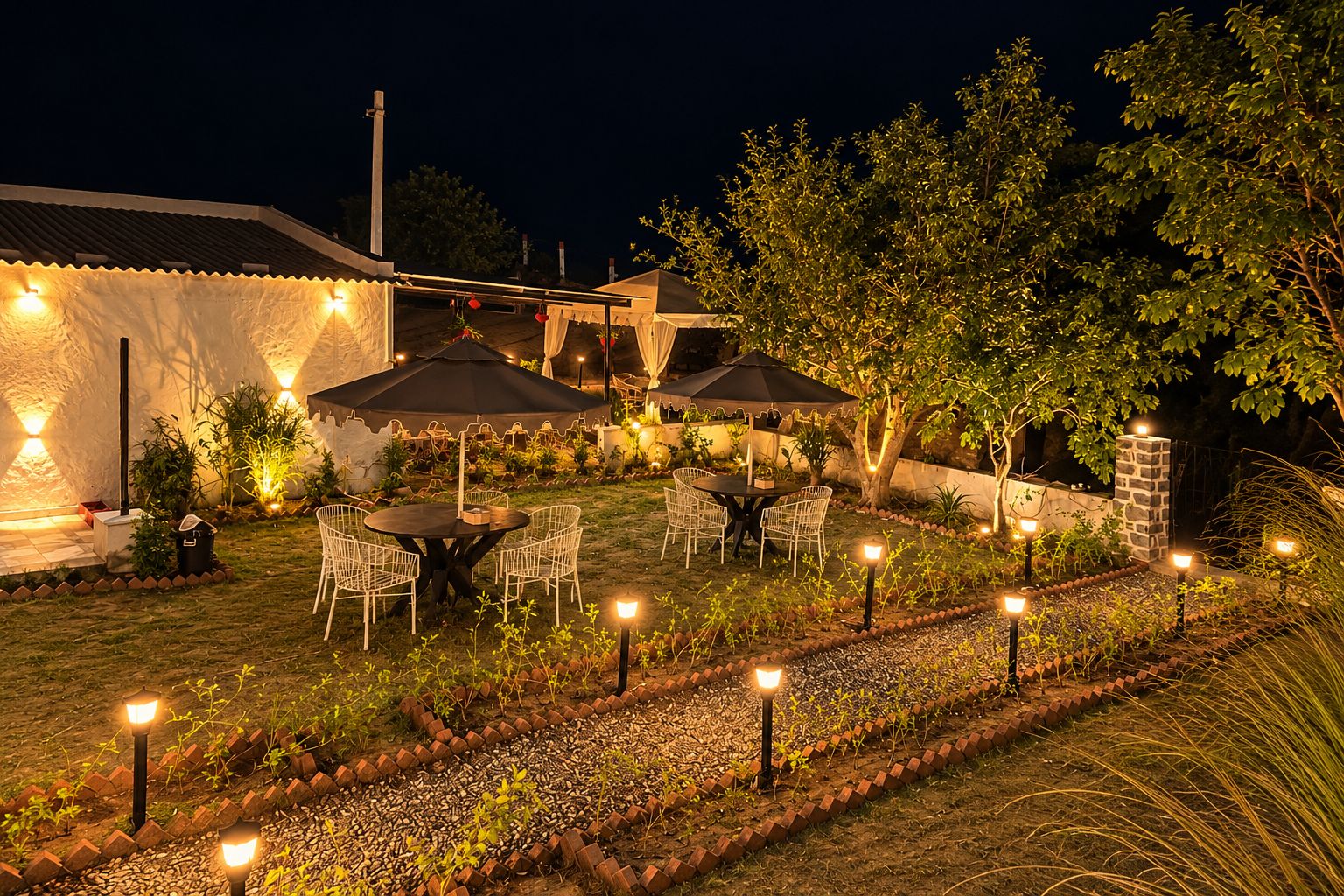 Un área de patio al aire libre con mesas y sillas, rodeada de plantas e iluminación decorativa.