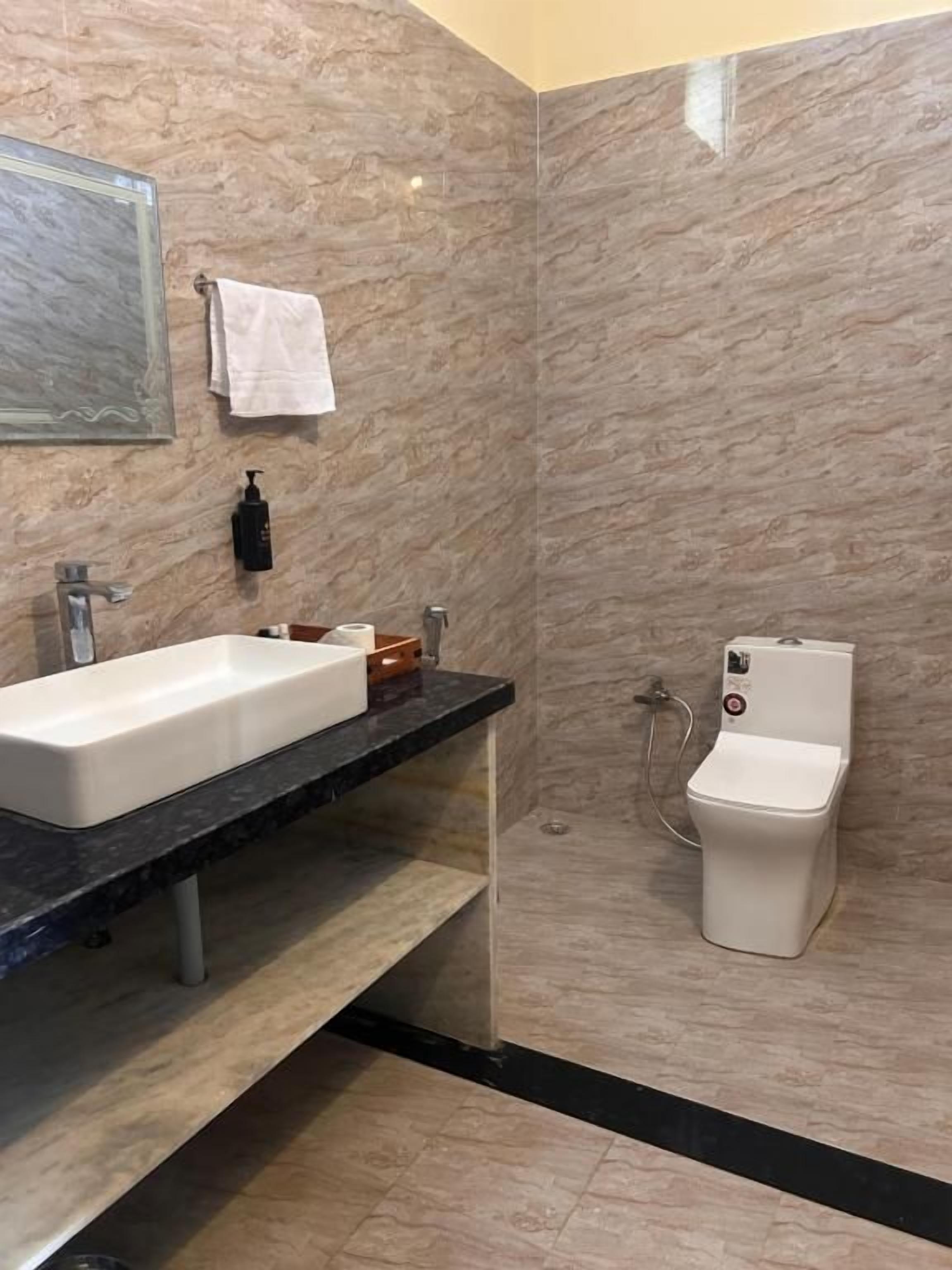 Un bagno con parete in marmo, lavandino bianco, servizi igienici e doccia.