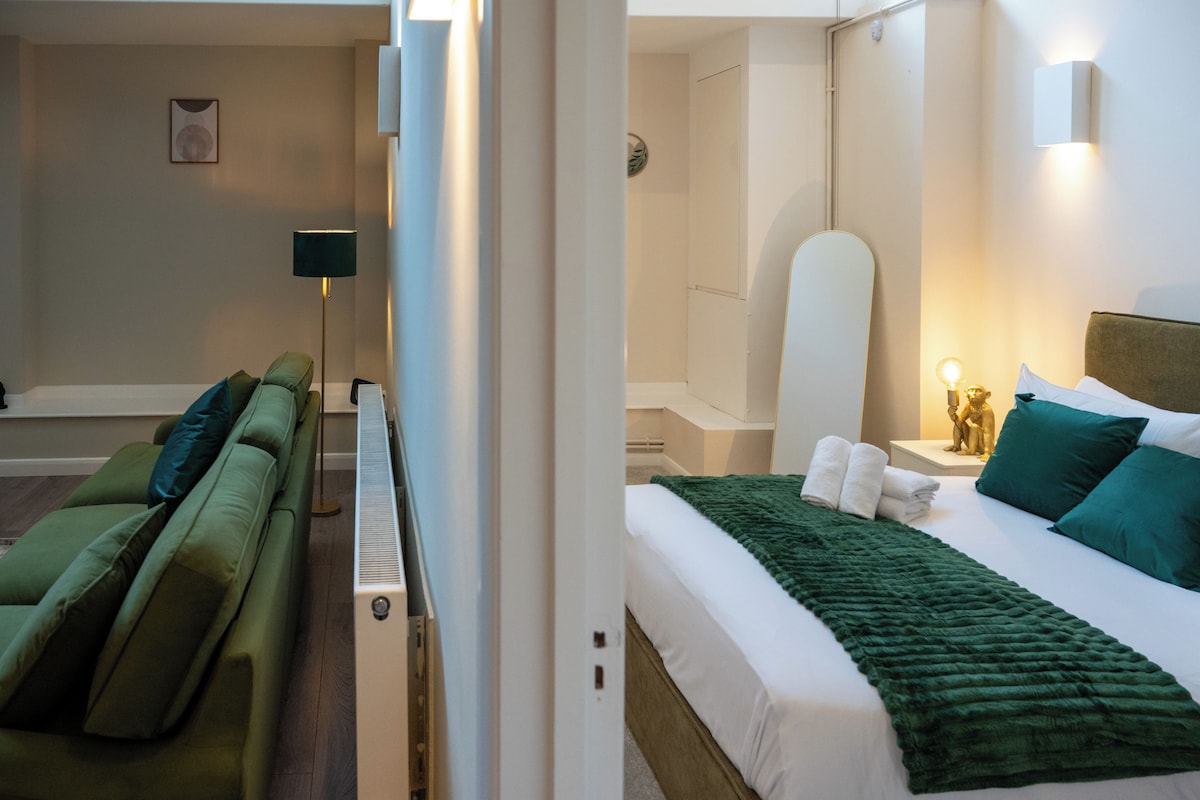 A hotel room with a bed, a green sofa, a standing heater, and a shower area.