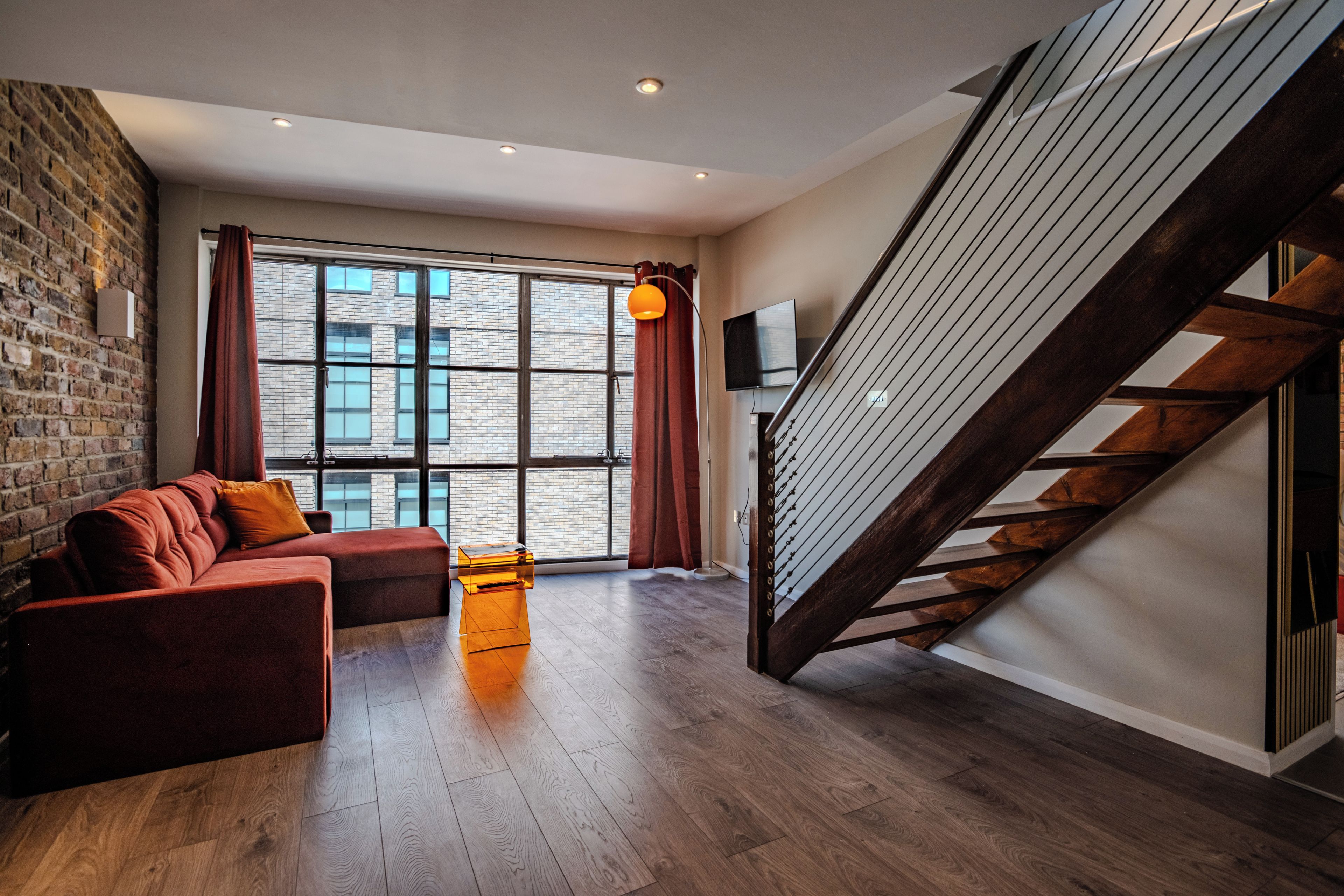 Ein modernes Wohnzimmer mit Backsteinwand, einer Couch, einem Couchtisch und einer Treppe.
