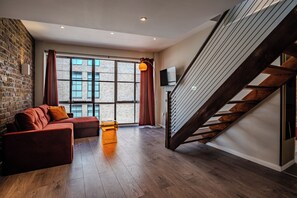 Una sala moderna con pared de ladrillo, un sofá, una mesa de centro y una escalera.