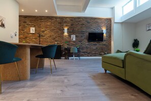 Una sala moderna con pared de ladrillo, un televisor de pantalla plana sobre una mesa de comedor de madera y un sofá verde.