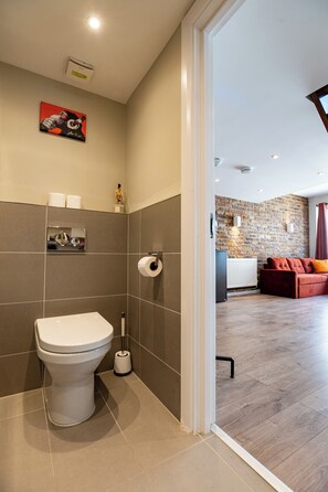 A modern bathroom with a toilet, a hand dryer, and a roll of toilet paper on the wall. - Eagle Wharf Grand Residences (London)