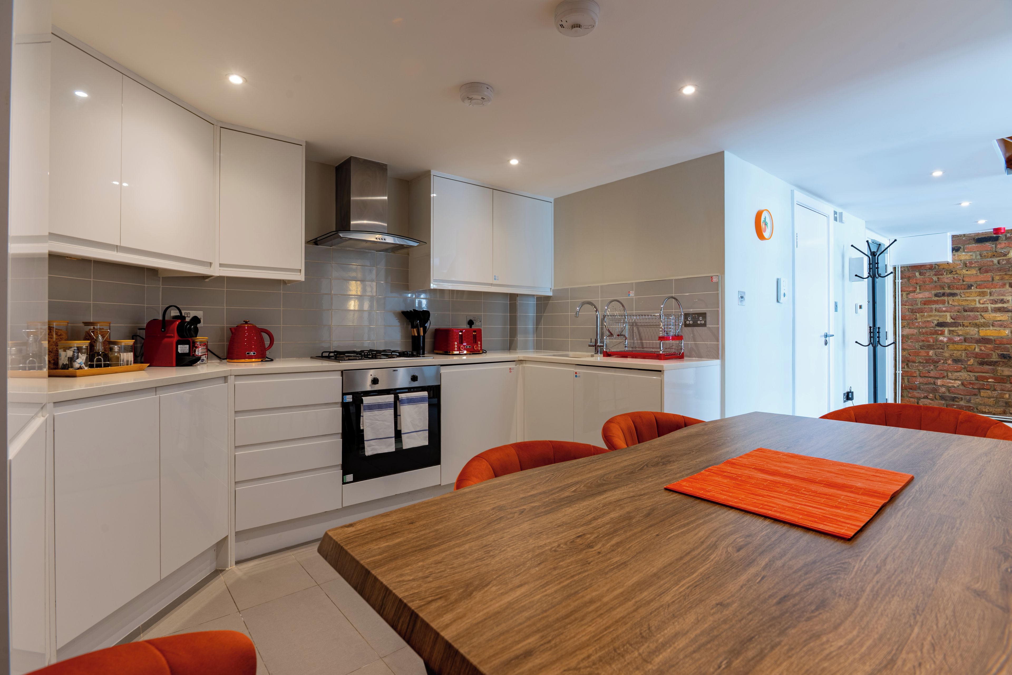 Eine moderne Küche mit weißen Schränken, einem Holzespeisetisch und orangefarbenen Stühlen.
