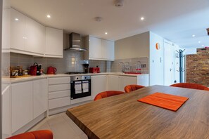 Una cocina moderna con armarios blancos, una mesa de comedor de madera y sillas color naranja.