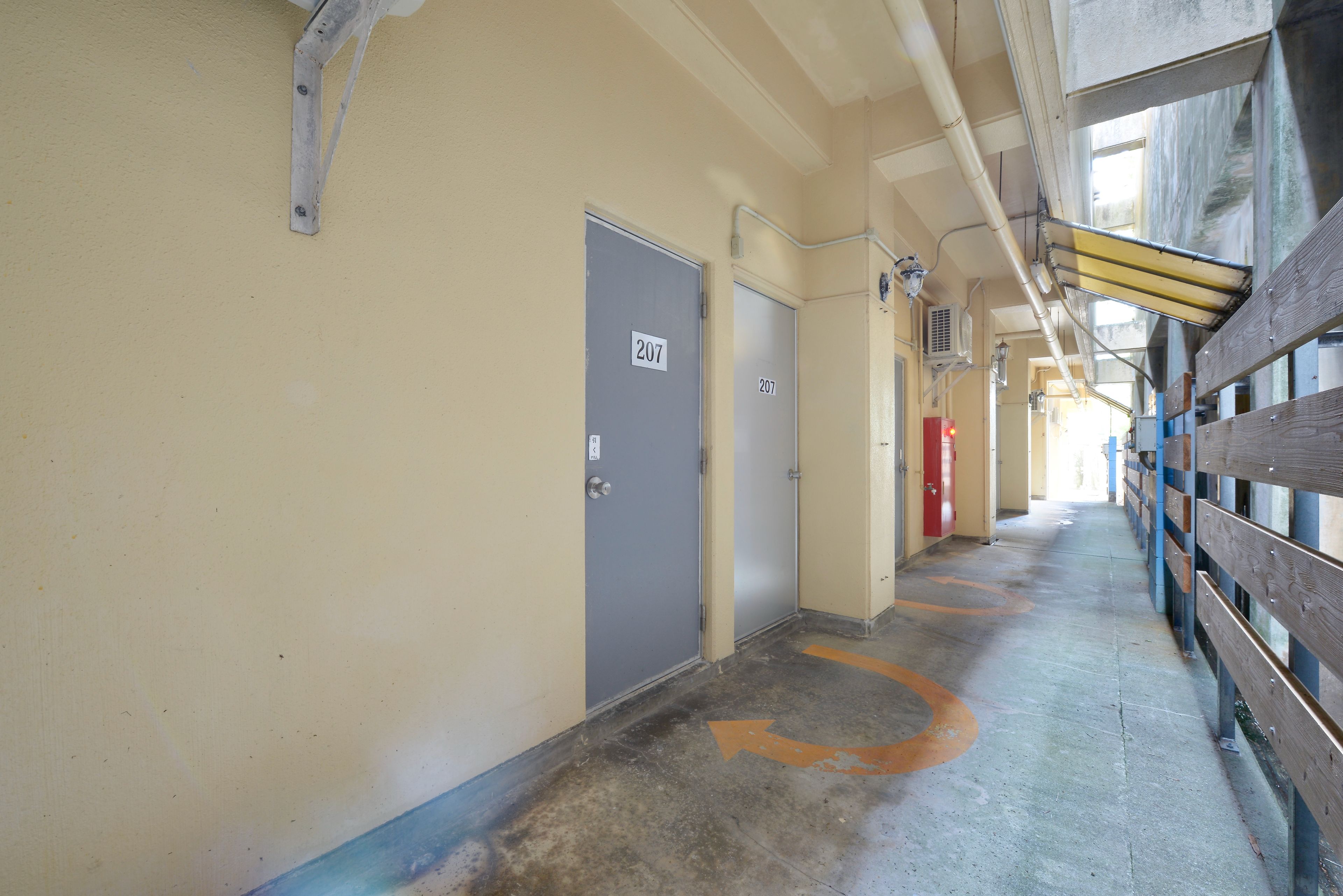 A corridor with doors marked 207, a wooden fence on the right, and a concrete floor with directional arrows.