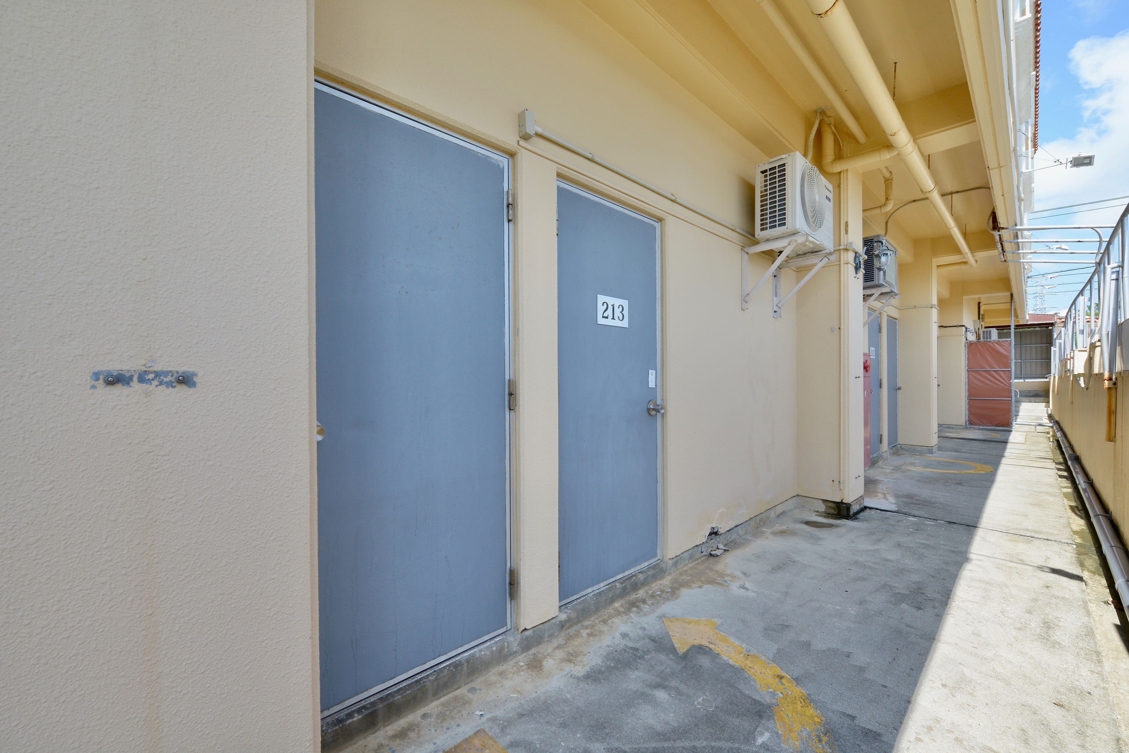 Um corredor com duas portas, uma delas com o número 213, e um aparelho de ar condicionado fixado na parede.