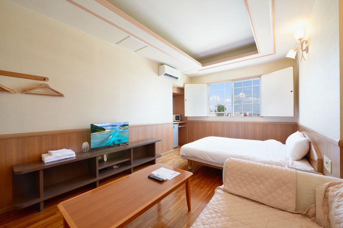 A hotel room with a bed, a TV, a desk, and a window.