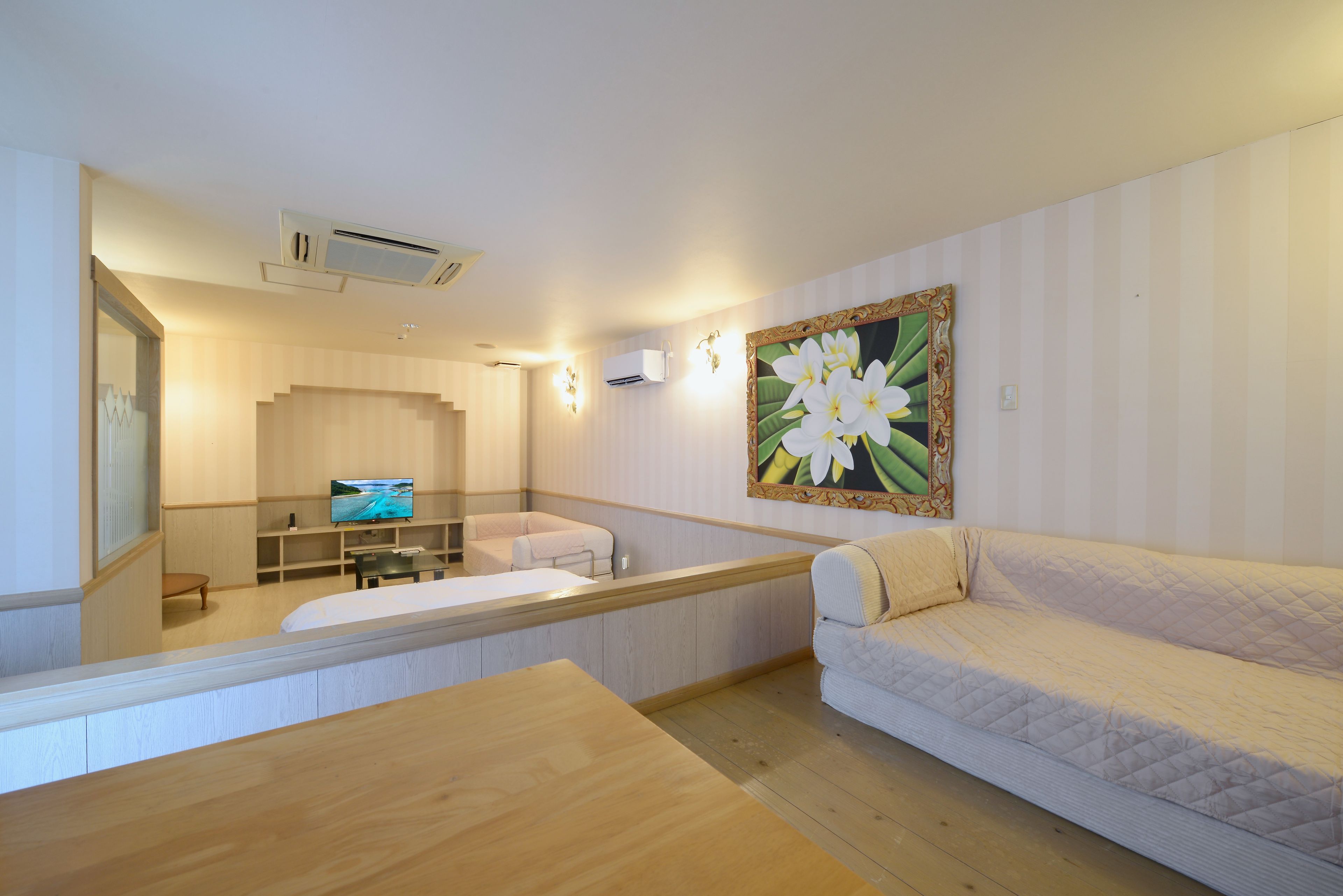 A hotel room with a bed, a sofa, a TV, and a painting on the wall.