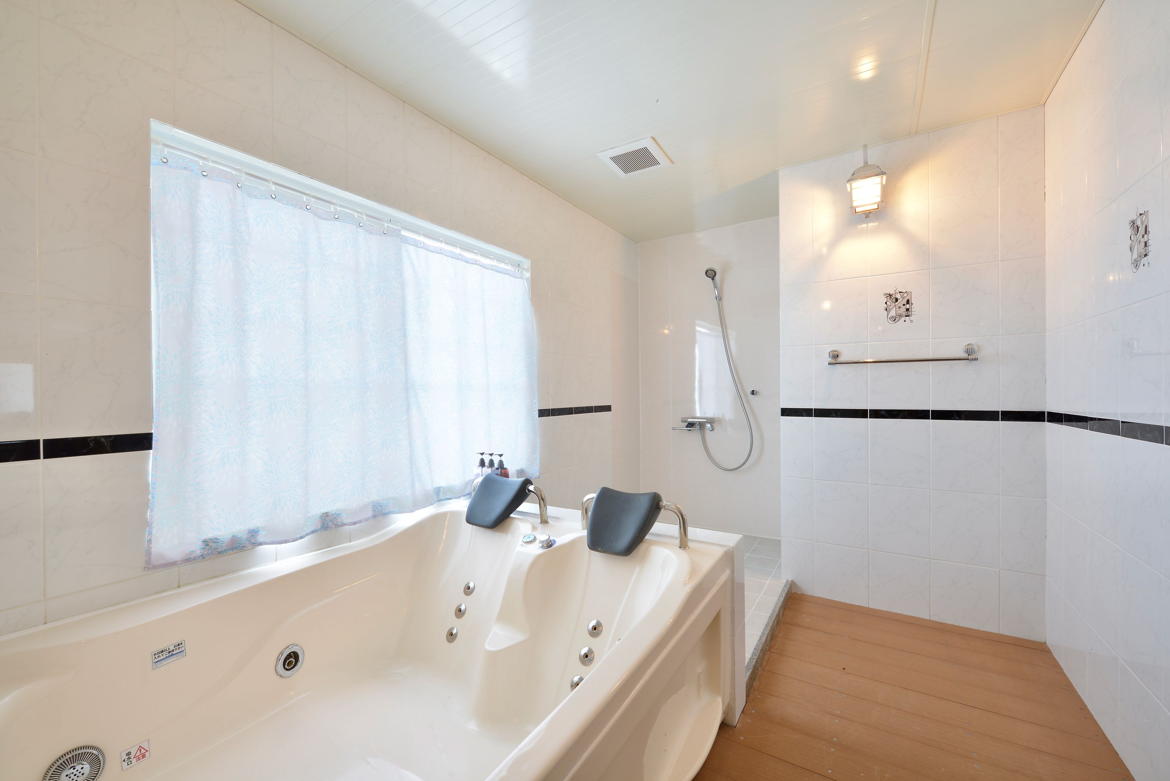 A modern bathroom with a bathtub, shower, and a window with a curtain.