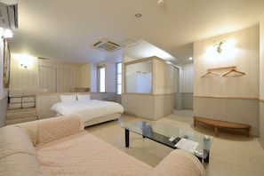 A hotel room with a bed, a sofa, a glass table, a bench, a wardrobe, and a mirror. - Hotel JUNCTION  (Okinawa-shi)