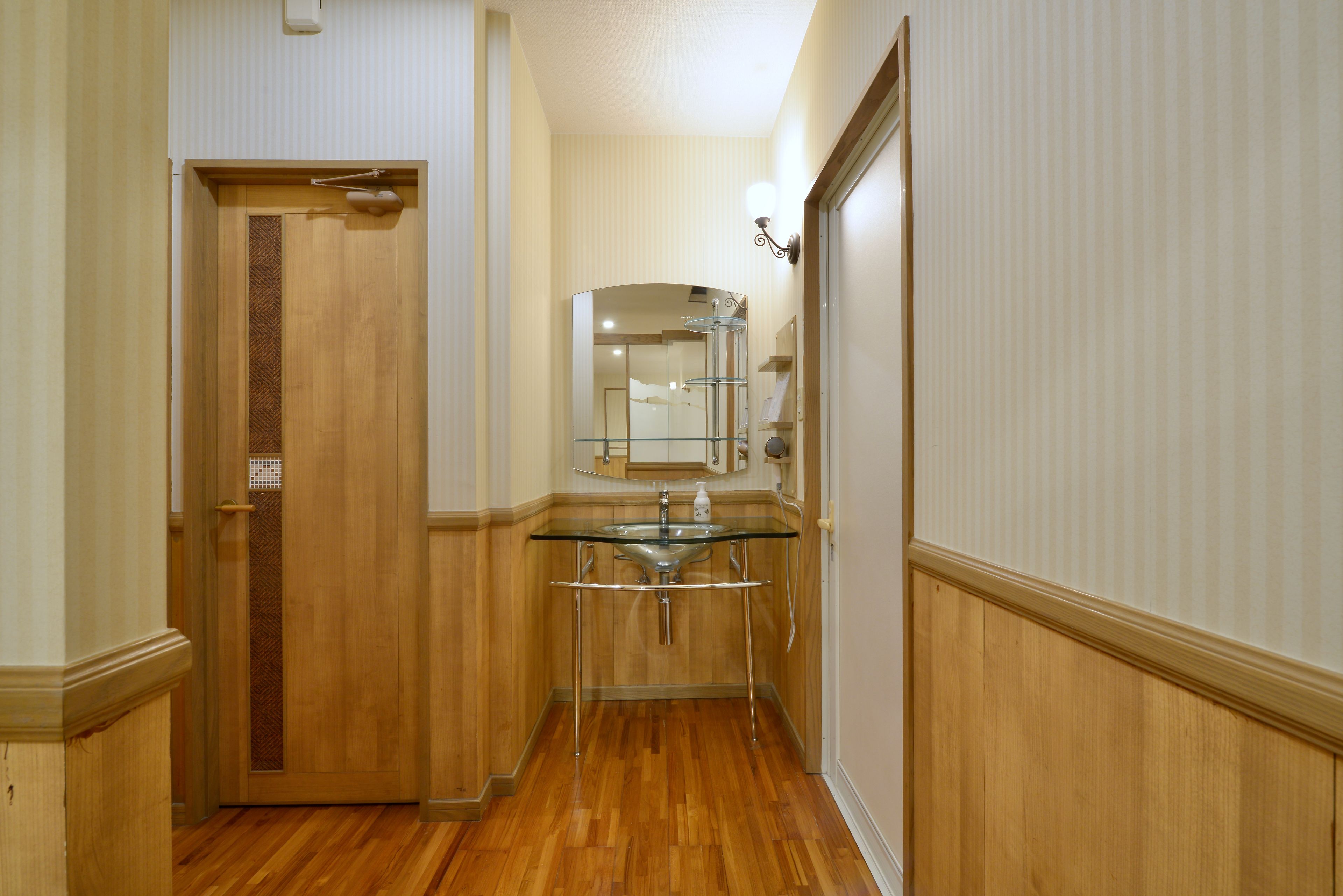 A hallway with wooden flooring, a glass sink, and a mirror above it.